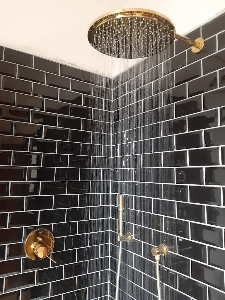 Douche à l'italienne carrelée en métro noir avec pomme de pluie dorée, réalisée par YR Sanitaire & Chauffage à Tournai