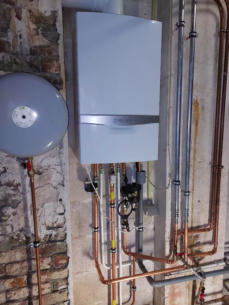 Chaudière murale Vaillant et tuyauteries en cuivre dans une cave, réalisation YR Sanitaire & Chauffage à Ath